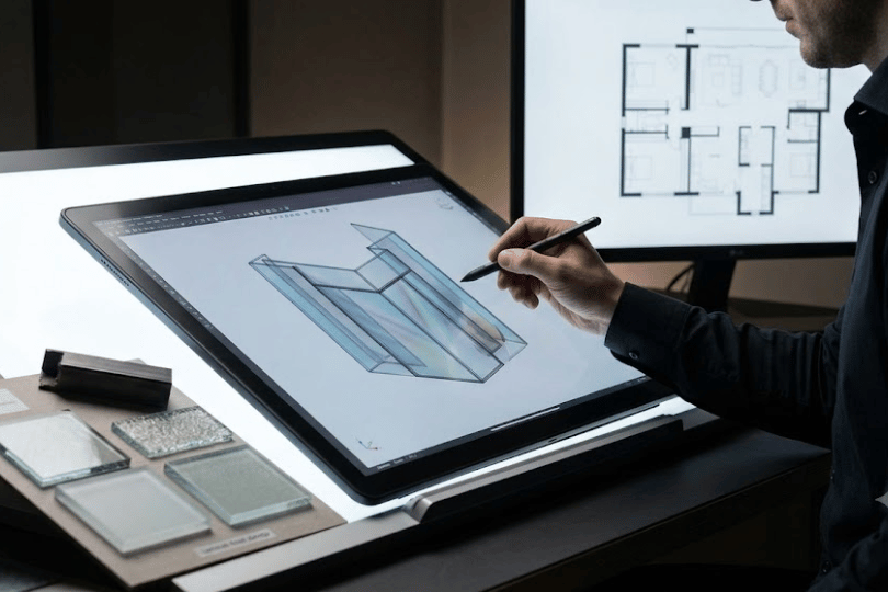 Architectural glass designer creating a 3D CAD model on a digital drawing tablet with glass material samples.