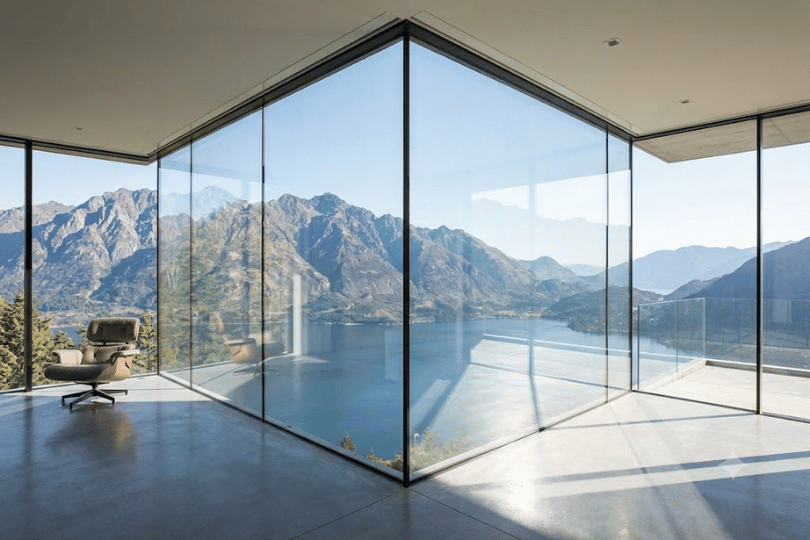 Minimalist living room with floor-to-ceiling custom glass walls overlooking a mountain lake
